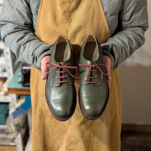 靴作り教室でAさんが2足目に制作した深緑のダービーシューズを手に持つ写真