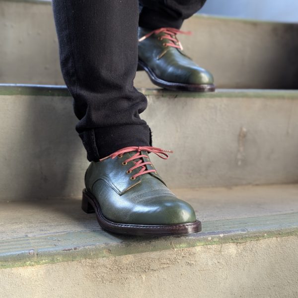 深緑の革靴を履いて一歩踏み出した瞬間の足元右側面